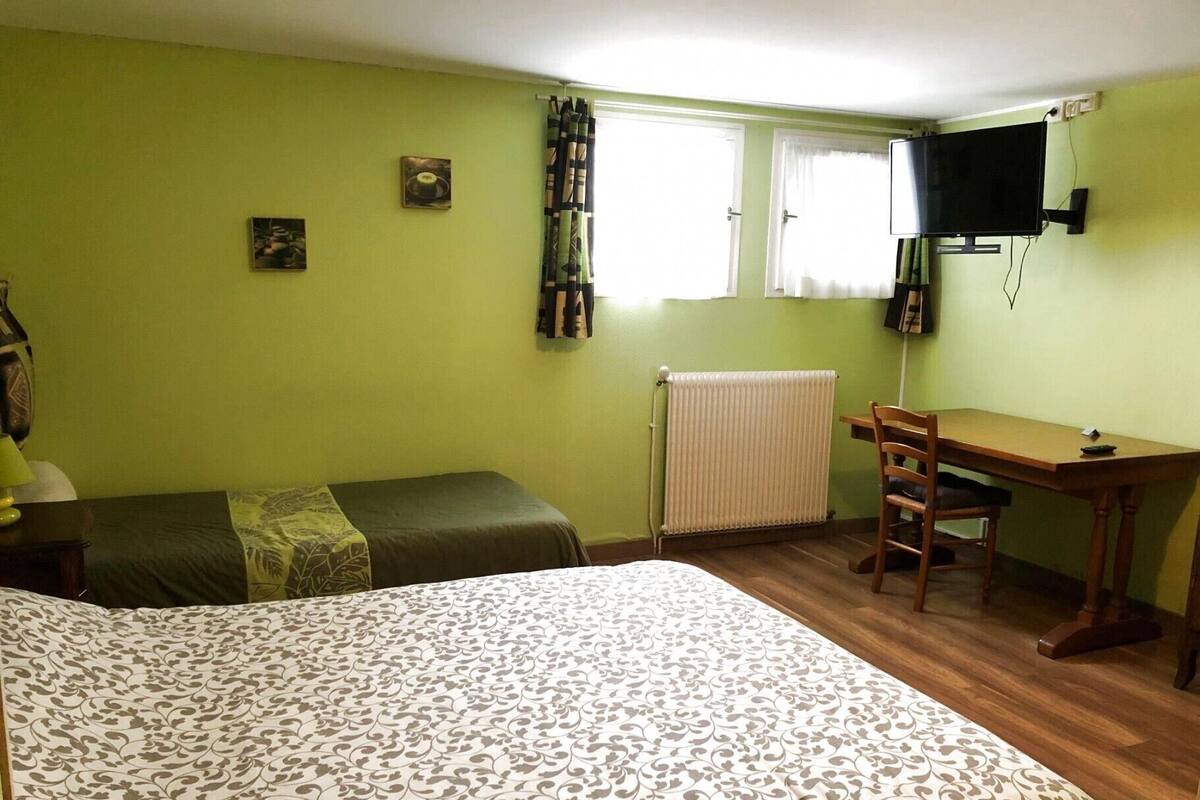 A room with a large bed, a desk, a chair, a radiator, and a television on the wall.
