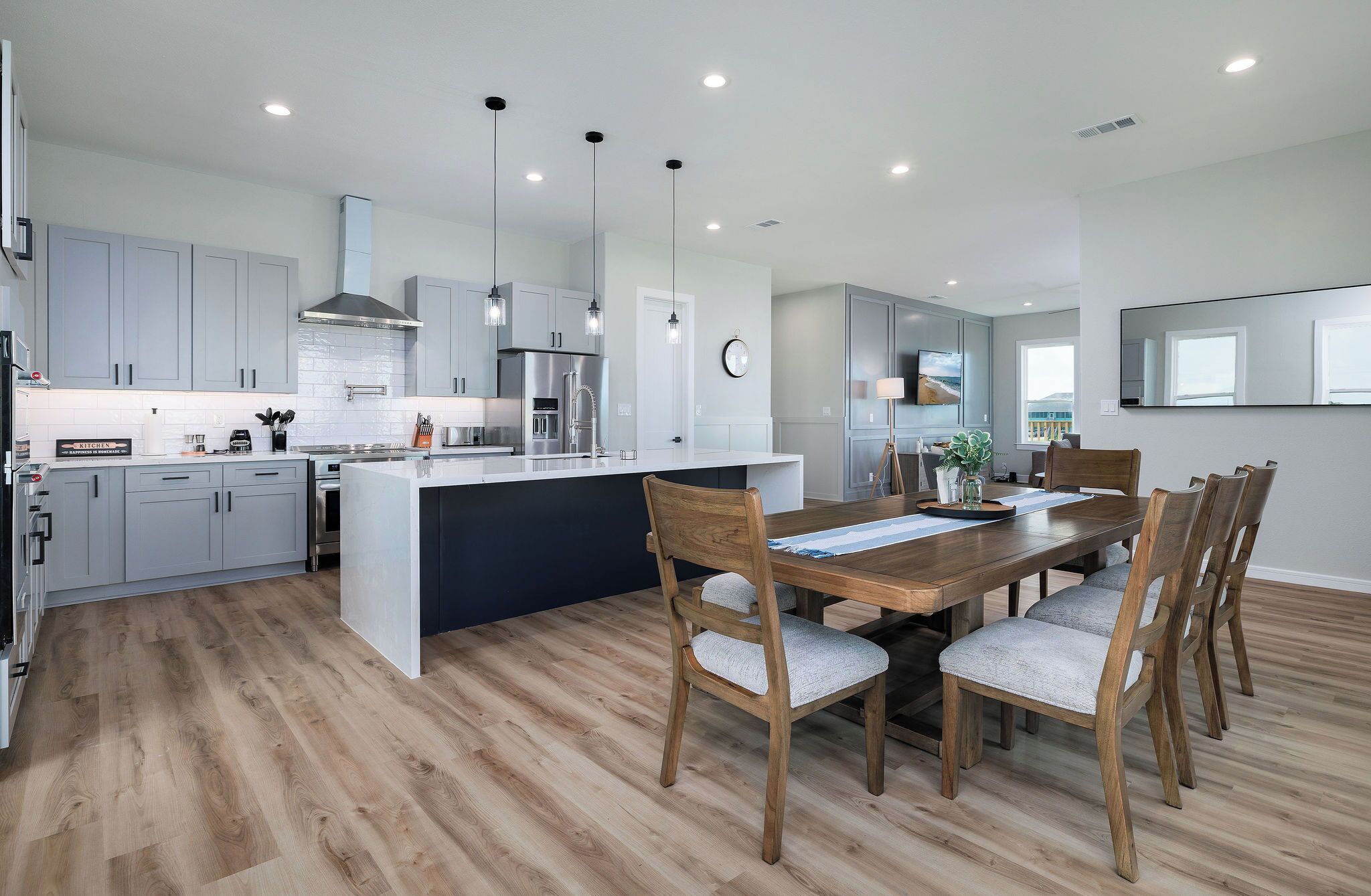 A modern kitchen with grey cabinets, a central island, and a dining area with wooden chairs and a table.