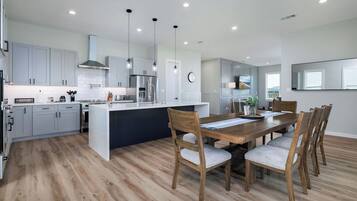 Una cocina moderna con armarios grises, una isla central y un comedor con sillas y una mesa de madera.