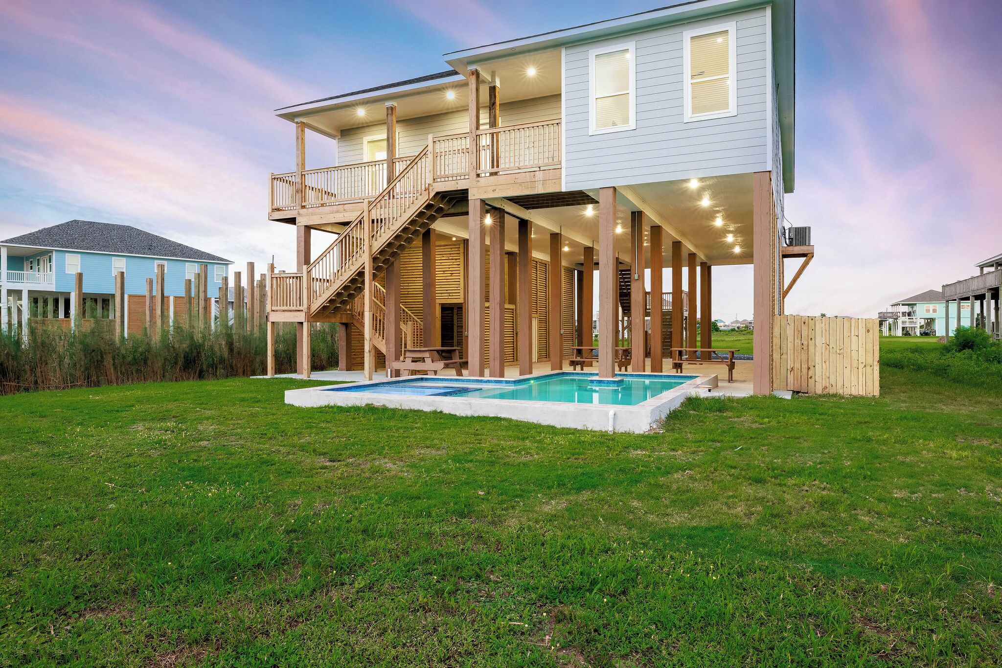 A two-story house with a wooden deck, a staircase, and a swimming pool.