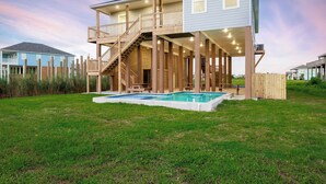 Ein zweistöckiges Haus mit einer Holzterrasse, einer Treppe und einem Schwimmbecken.