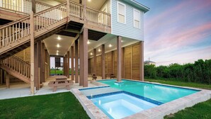 Ein zweistöckiges Haus mit einer Holztreppe, einer überdachten Terrasse und einem Swimmingpool.