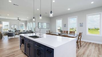 Una cocina amplia con una isla grande, luces colgantes modernas y vistas al exterior.