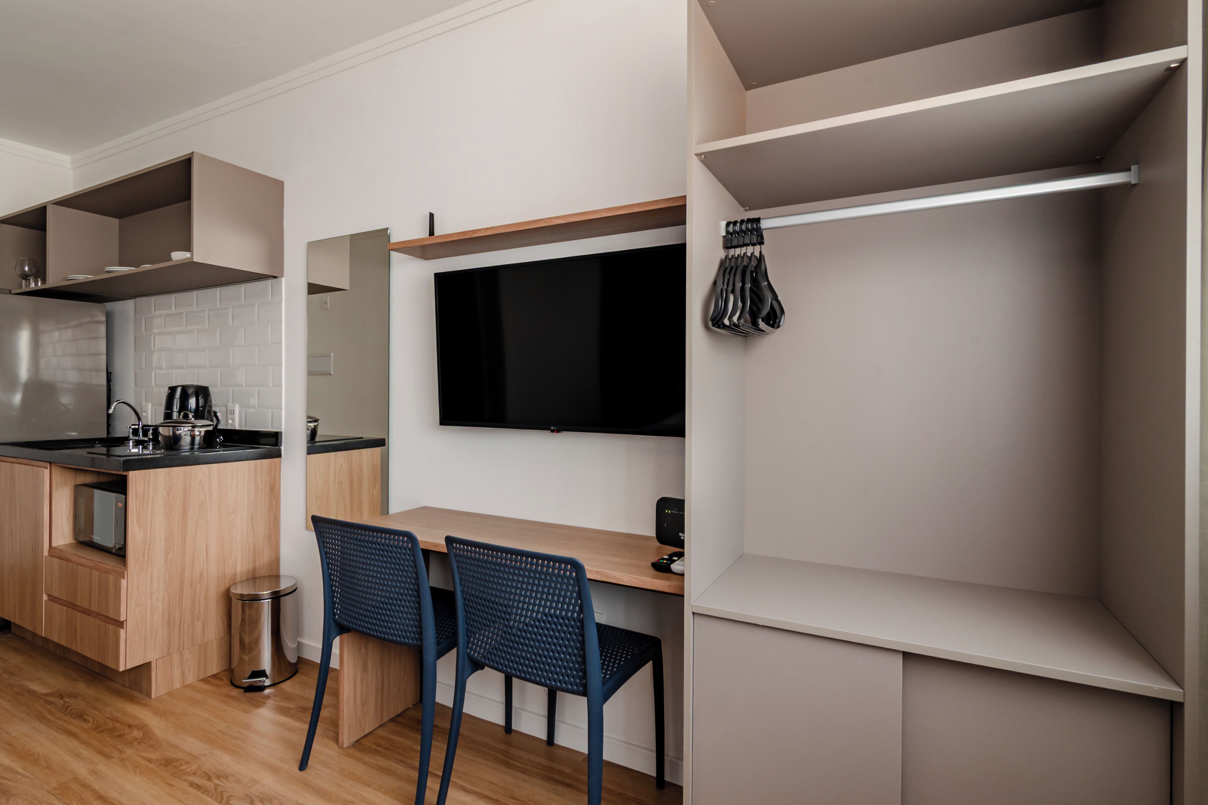 Uma cozinha moderna com fogão embutido, sala de jantar com duas cadeiras e uma TV fixada na parede.