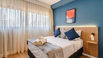 Ein modernes Schlafzimmer mit Bett, Vorhängen, einer Wandleuchte und Blick auf die Stadt.