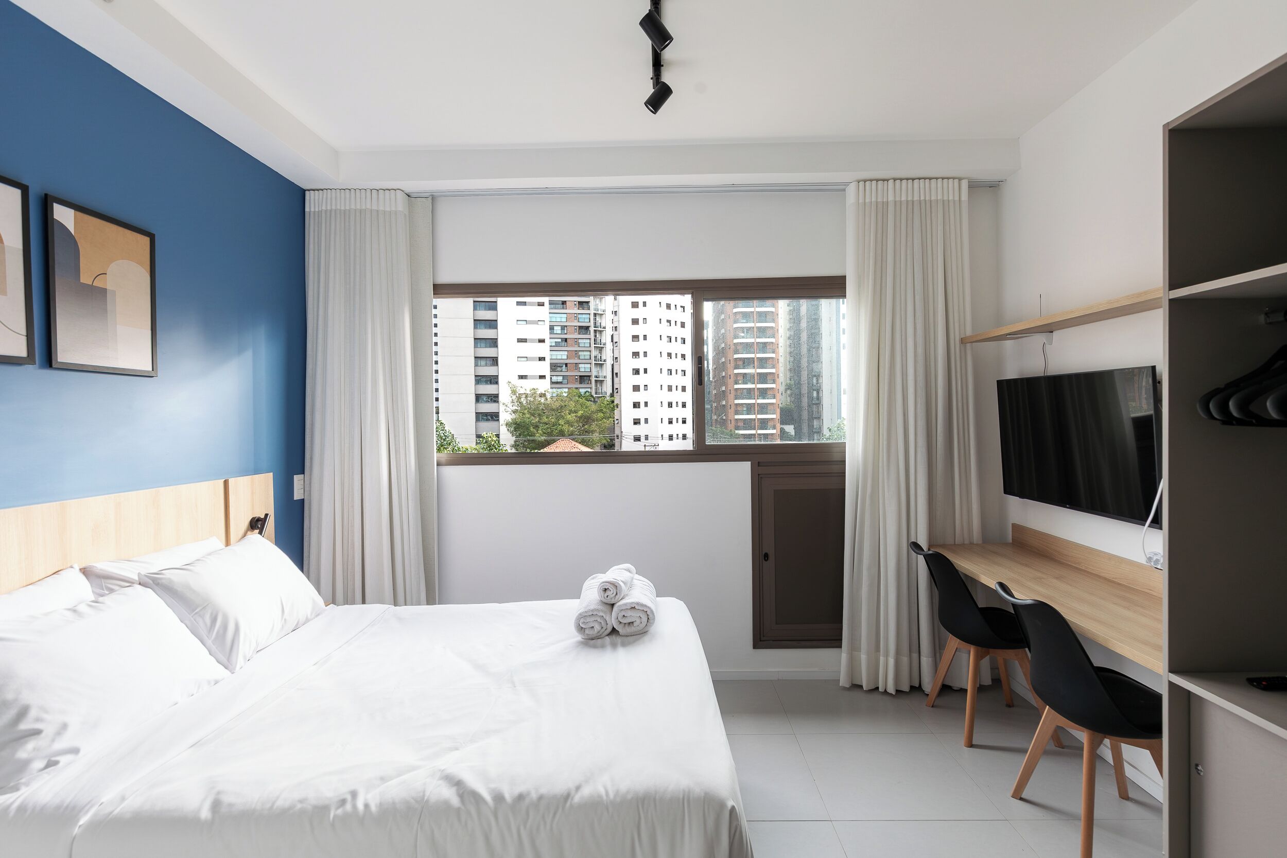 Een hotelkamer met een bed, een bureau met stoel, een televisie en een raam met gordijnen.