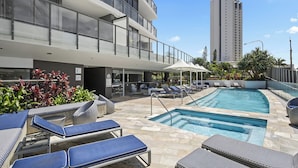 A rooftop pool area with lounge chairs, a swimming pool, and a tall building in the background. - Seabright Nook Resort Perks and Sky Views by the Sea (Surfers Paradise)