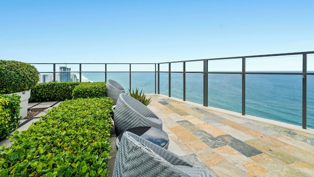A balcony with wicker furniture, a stone-tiled floor, and a view of the sea and city skyline. - Seabright Nook Resort Perks and Sky Views by the Sea (Surfers Paradise)