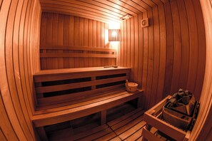 Una sauna in legno con panche e un sedile, un riscaldatore a parete e un contenitore di pietre.