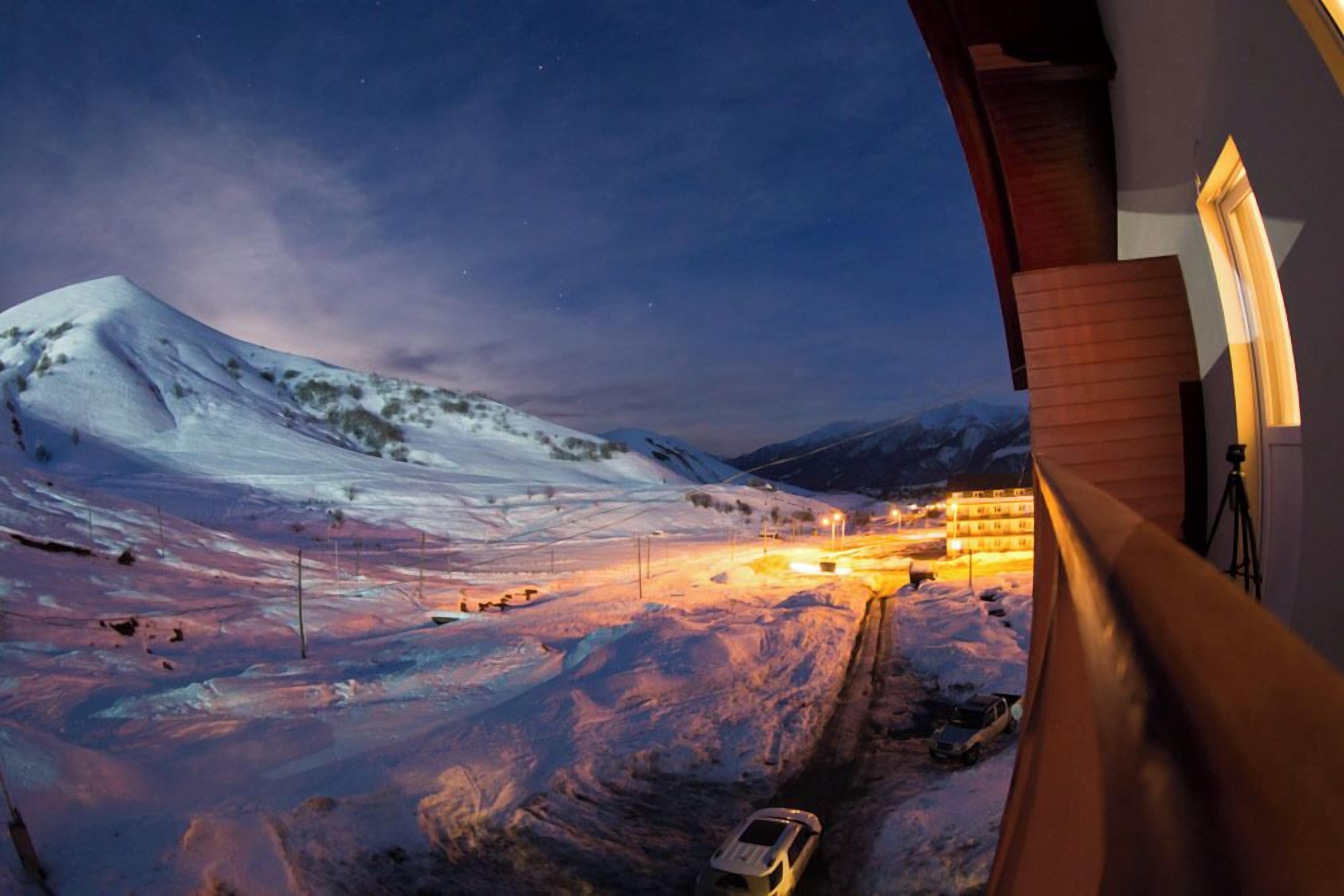 A snowy mountain landscape at twilight with a building in the foreground.