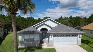 A single-story house with a garage, a small attached shed, and a palm tree in the front yard. - NEW - Free pool-/spa heat near Disney (Kissimmee)