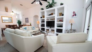 A living room with a sofa, coffee table, TV, and shelves. - NEW - Free pool-/spa heat near Disney (Kissimmee)