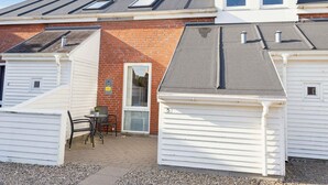 A row of white mobile homes with grey roofs and skylights, a small patio with a table and chairs, and a brick wall.