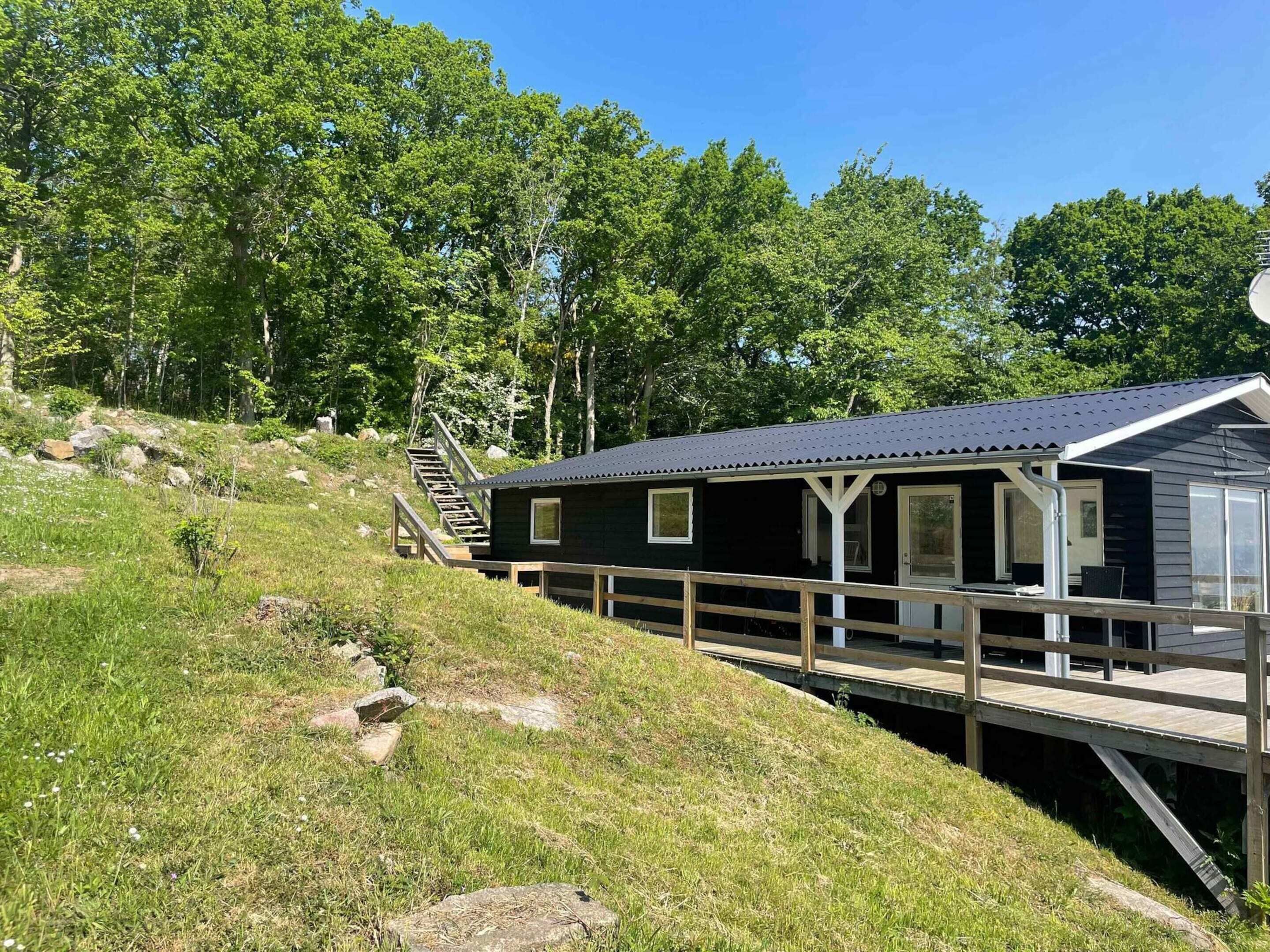 A cabin with a deck and a staircase leading up to it, surrounded by greenery.