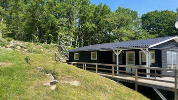 A cabin with a deck and a staircase leading up to it, surrounded by greenery.