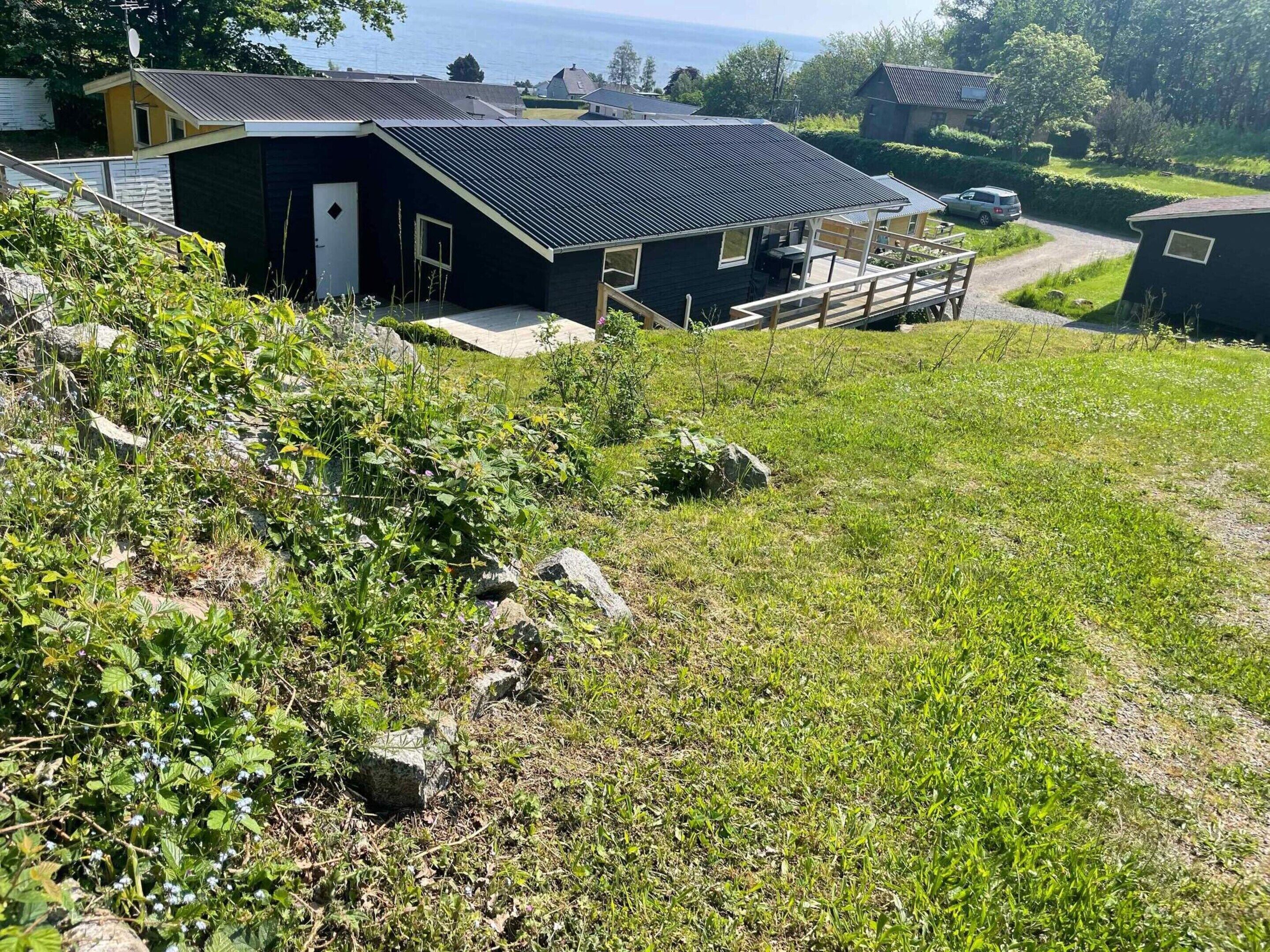A hillside view of a house with a metal roof, a deck, and a view of the sea.