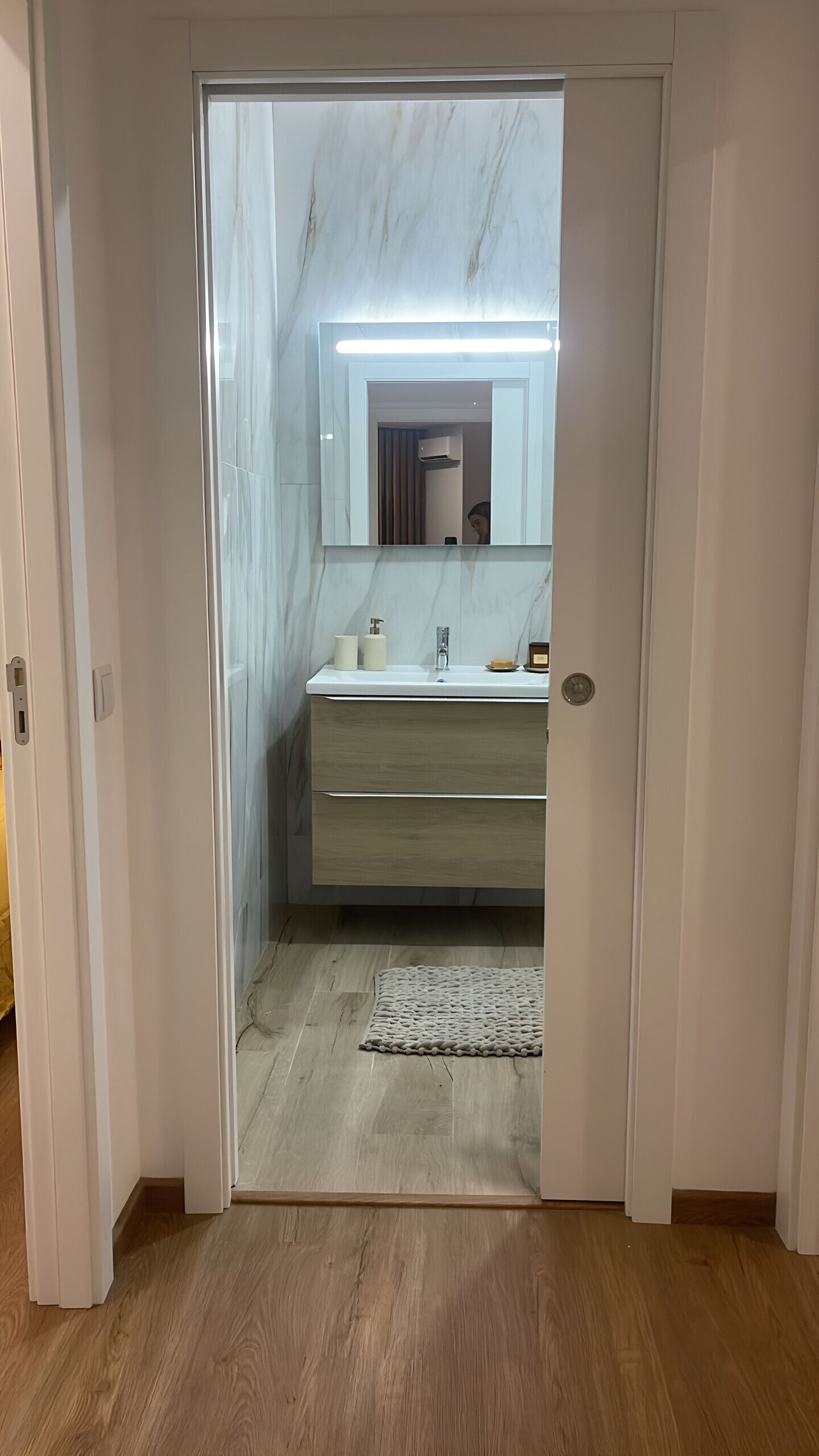 A modern bathroom with a marble vanity, a mirror, and a lighted vanity area.
