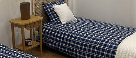 A simple, clean room with a single bed, a nightstand with a lamp, and a plain wall.