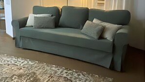 Un soggiorno con divano, lampada da terra, tappeto decorato e finestra con tende.