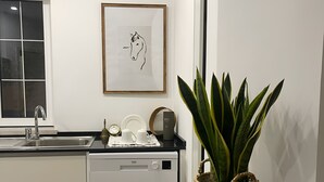 Una cucina moderna con lavastoviglie, lavello e finestra. Una cornice con un'immagine appesa al muro e un vaso con una pianta su un tavolino.
