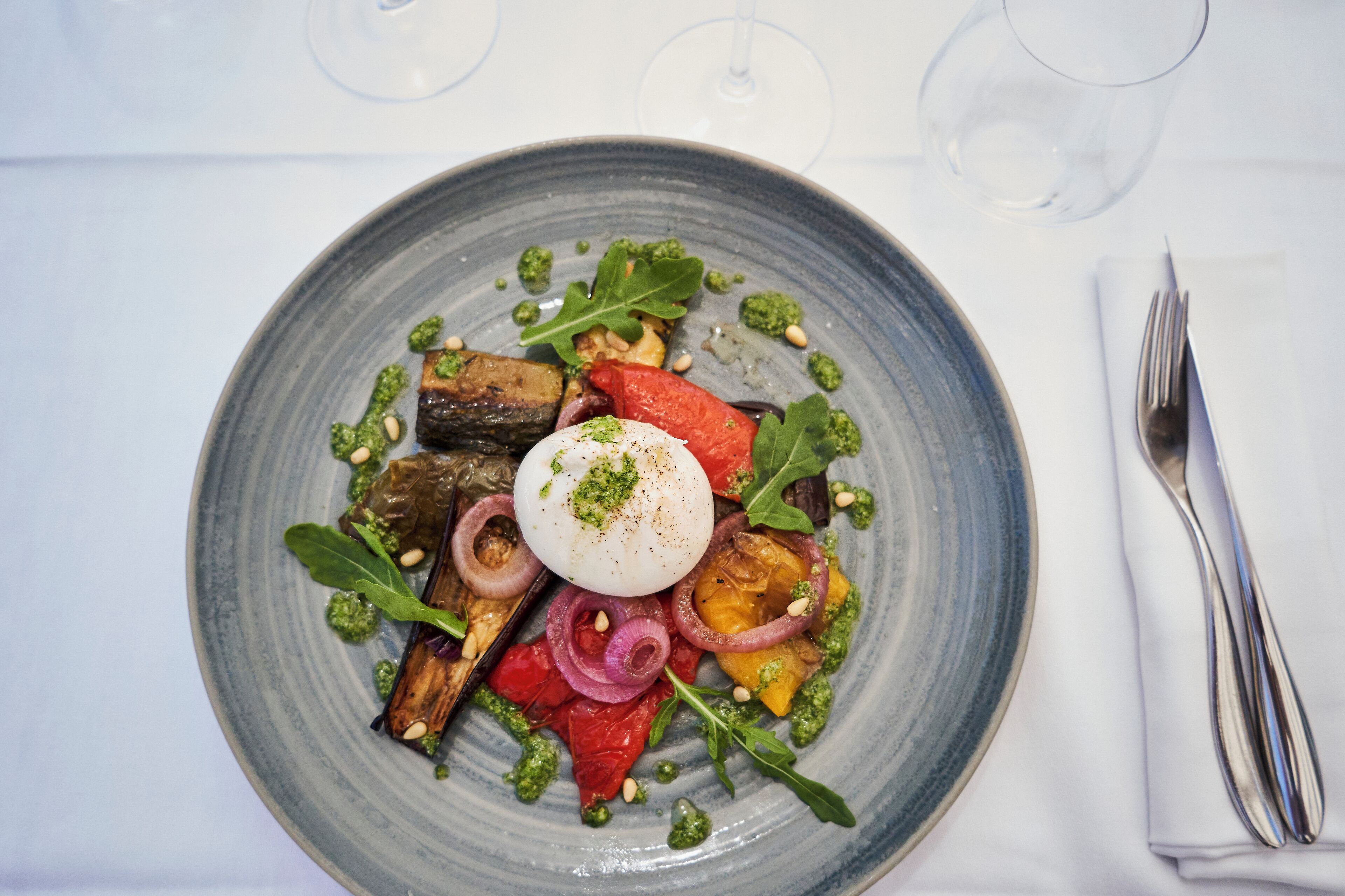 Une assiette bleue contenant un plat composé d’un œuf poché, de légumes et de verdure.