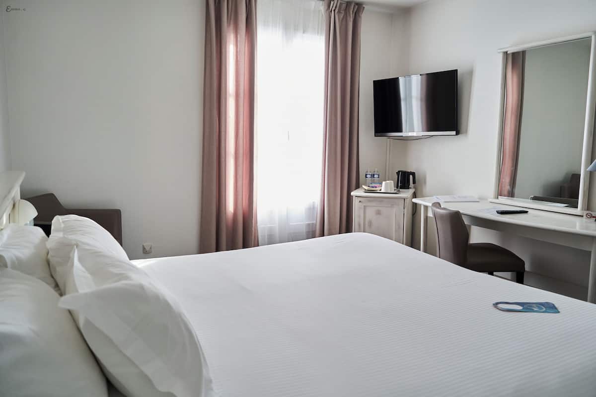 A hotel room with a bed, a desk, a chair, a television, and a window with curtains.