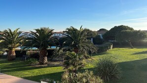 A well-maintained garden with palm trees and a neatly trimmed lawn, leading to a building with a tiled roof. - THALACAP Ile de Ré (Ars-en-Ré)