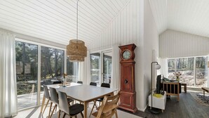 Une salle à manger spacieuse, dotée d’une grande table et de chaises, d’une imposante horloge comtoise et de grandes fenêtres offrant une vue sur l’extérieur.