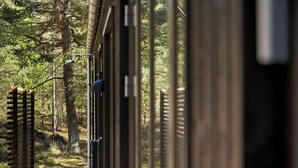 Une terrasse en bois avec des garde-corps en métal, entourée d’arbres.