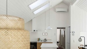 Une cuisine moderne avec des meubles blancs, un îlot central, des luminaires suspendus et une vue sur l’espace repas.
