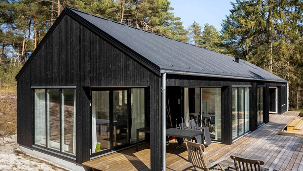 Une cabane moderne dotée d’une grande terrasse, de larges fenêtres et d’une façade en bois.