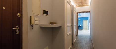 A narrow hallway with a wooden door on the left, a white shelf with a bowl, and a blue wall at the end.