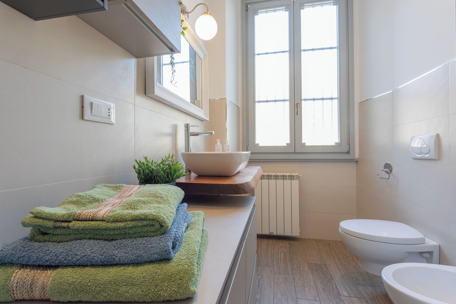 A modern bathroom with a white sink, a toilet, and a window providing natural light.