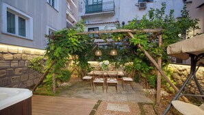A wooden deck with a hot tub, a pergola with climbing plants, and a stone wall.