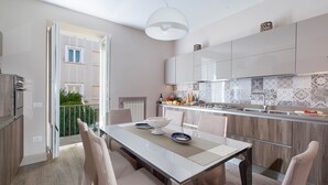 A modern kitchen with a dining area, featuring a large island, white cabinetry, and a view of the outdoors.