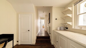 A hallway with a wooden floor, white walls, and a door at the end. Shelves are mounted on the wall, and a window is visible on the right. - Notting Hill Ground-Floor Retreat (London)