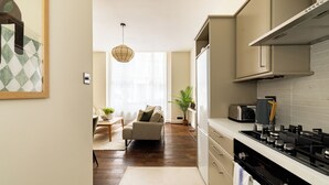 A modern kitchen with a gas stove, a built-in oven, and a microwave. There is a dining area with a sofa and a coffee table. - Notting Hill Ground-Floor Retreat (London)