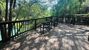 Una terraza de madera con sillas y barandilla, con vista a un cuerpo de agua, rodeada de árboles.