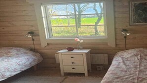A room with two beds, a small white dresser, a window with a view of trees and a field, and two floor lamps. - 4 Star Holiday Home in Ronne (Ronne)