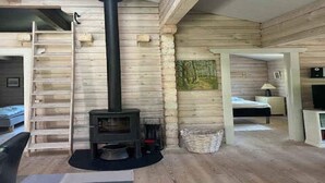 A log cabin interior with a central wood-burning stove, a ladder, a bed, and a painting on the wall. - 4 Star Holiday Home in Ronne (Ronne)