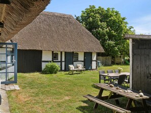 A thatched-roof house with a wooden door, a small garden, and a picnic table with stones. - 4 Star Holiday Home in Humble (Sydlangeland)