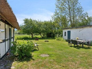 A rustic outdoor area with a thatched-roof building, a white structure with a window, and a table with chairs. - 4 Star Holiday Home in Humble (Sydlangeland)