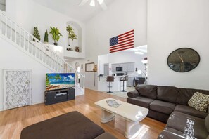 A spacious living area with a staircase, a flat-screen TV, a dining area, and a kitchen.
