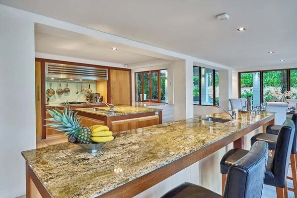 A modern kitchen with granite countertops, a central island, and a dining area with bar stools.