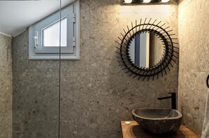 Ein Badezimmer mit einem Steinkonstruktion-Waschbecken, einem modernen Spiegel und einem Fenster mit weißem Rahmen.