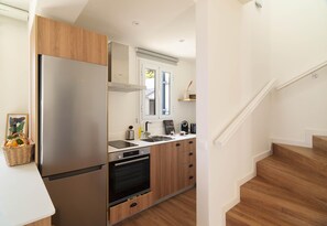 A modern kitchen with a stainless steel refrigerator, wooden cabinets, a built-in oven, and a wooden staircase.