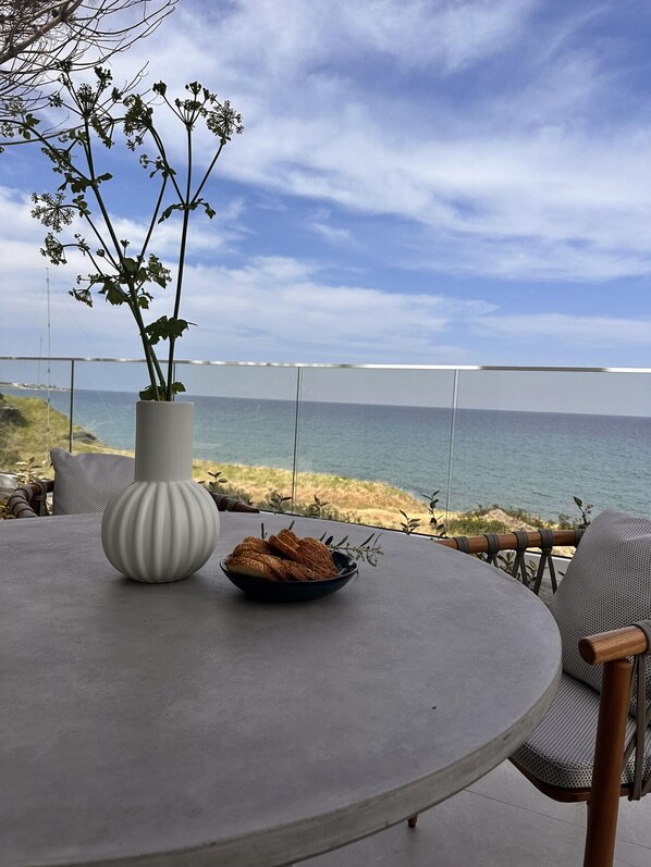 A round table with a white vase and a bowl of snacks, overlooking a beach and the sea.
