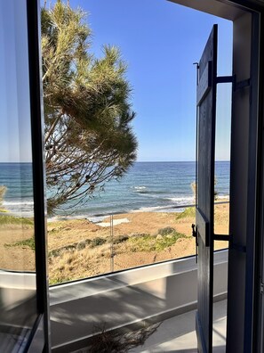 Blick aus einem Fenster auf einen Strand bei blauem Himmel.