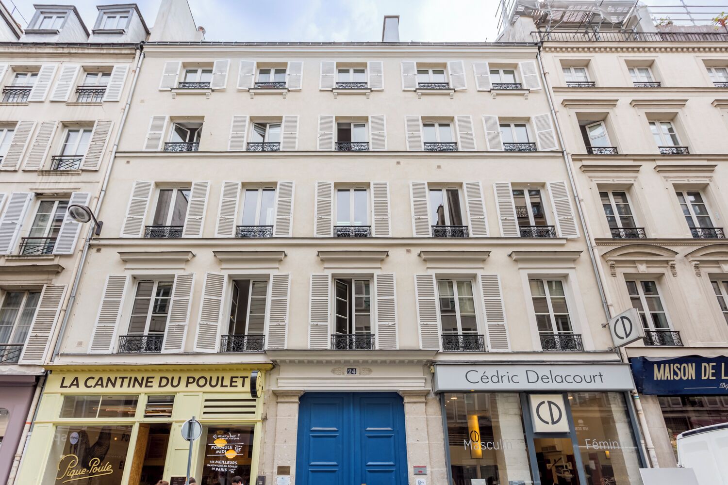 Un edificio de varios pisos con locales comerciales en la planta baja, incluyendo una farmacia y una boutique.