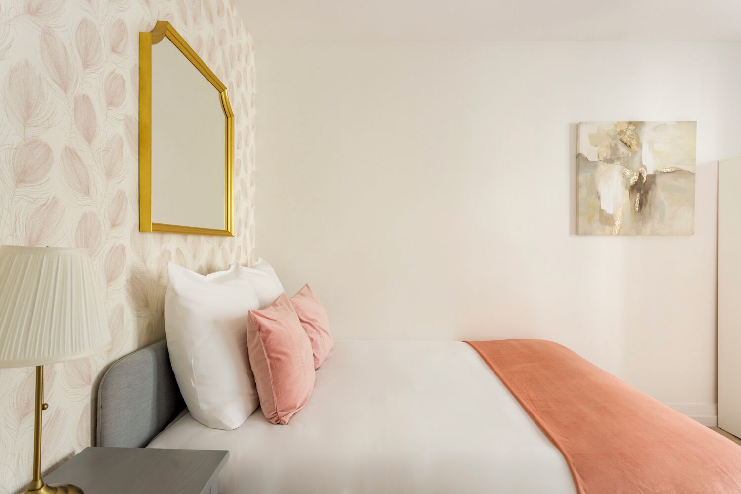 A neatly arranged hotel room with a bed, a bedside table, a lamp, and a wall-mounted mirror.